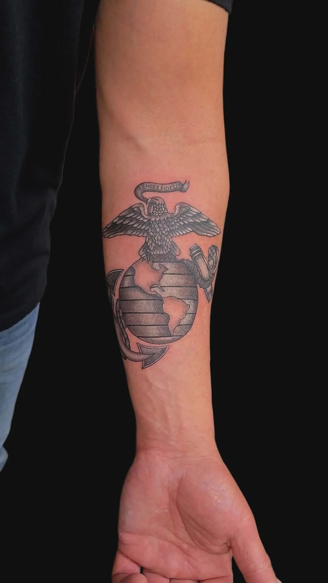 Tattoo of an eagle atop a globe with a banner reading 'Semper Fidelis' on a person's forearm.
