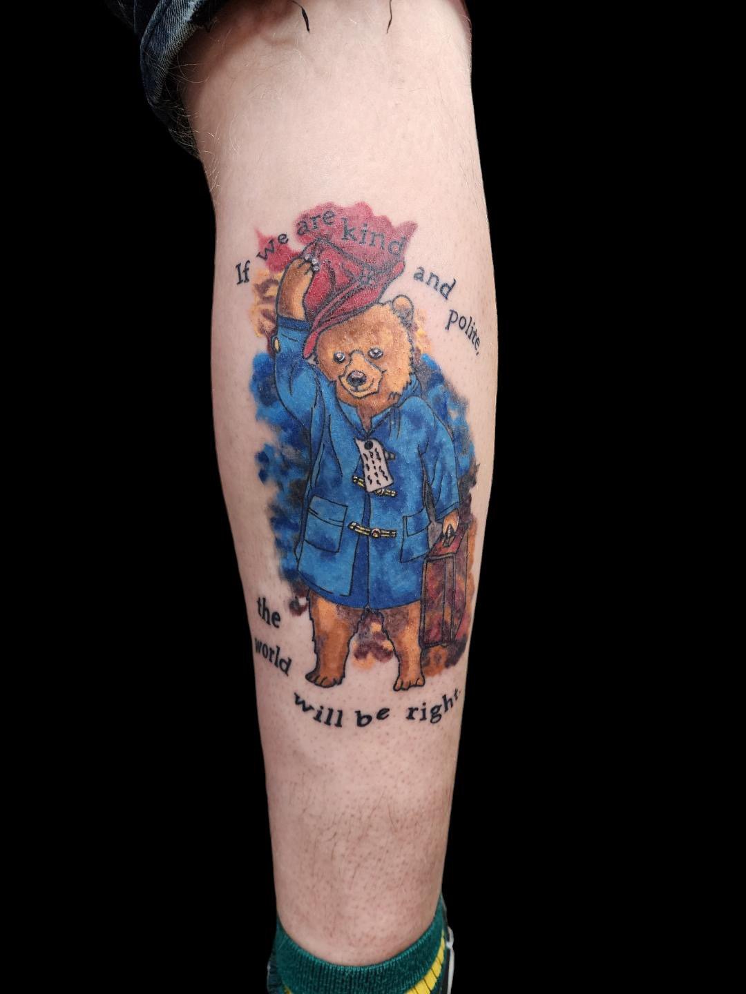 Colorful watercolor tattoo of a bear dressed as a police officer, holding a diploma and a briefcase, with the text 'If we are kind and polite, the world will be right' around it.