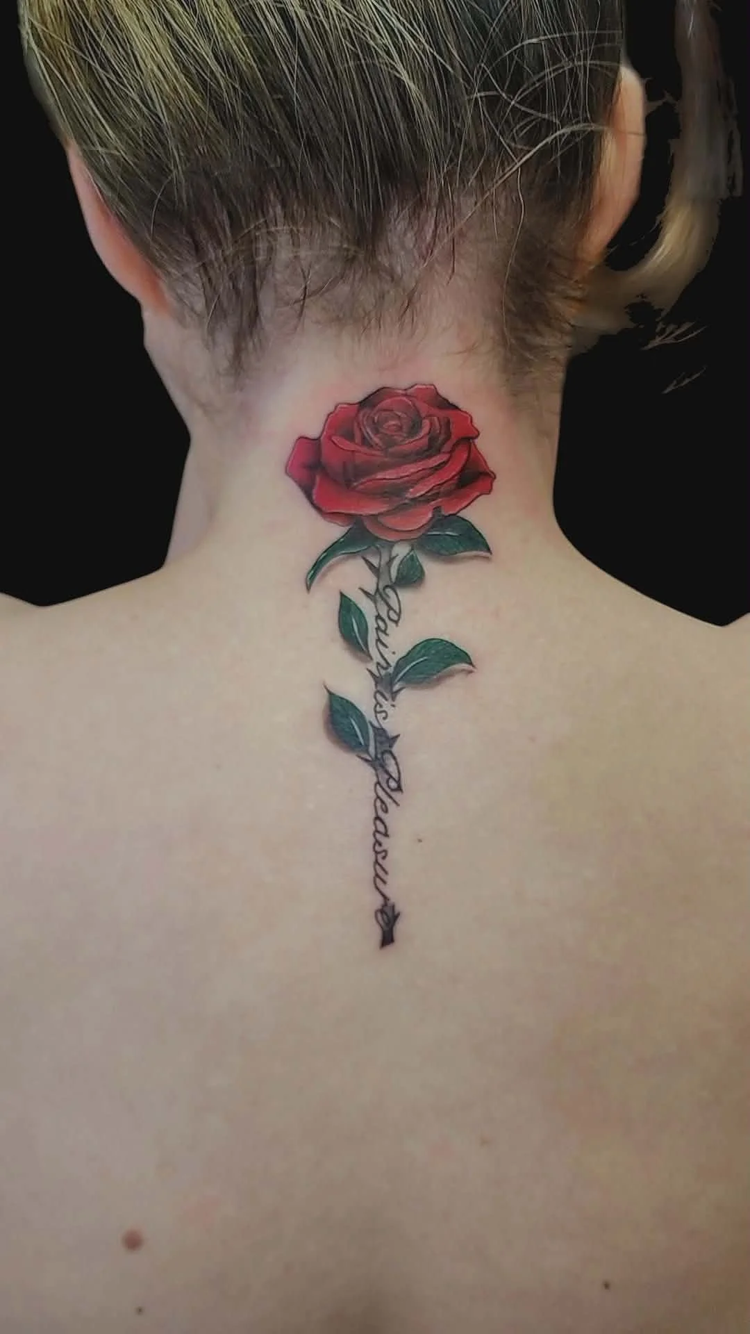 Tattoo of a red rose with green leaves on a person's upper back and neck, with the word "families" written in cursive.