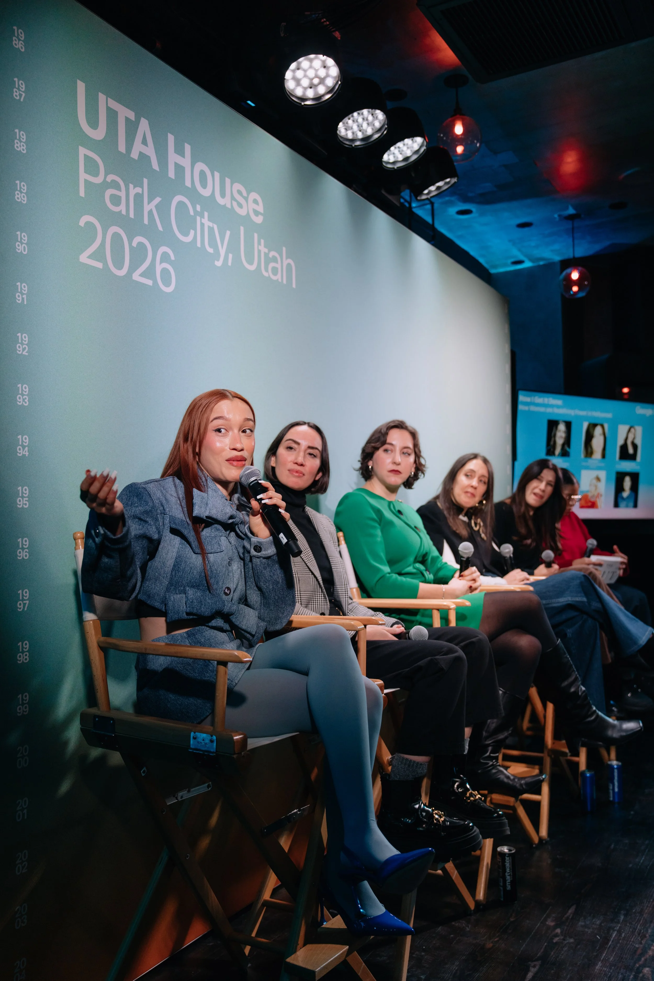 A panel discussion in Utah House, Park City, Utah, 2026, with five women sitting on stage with microphones, a large screen displaying their photographs on the right