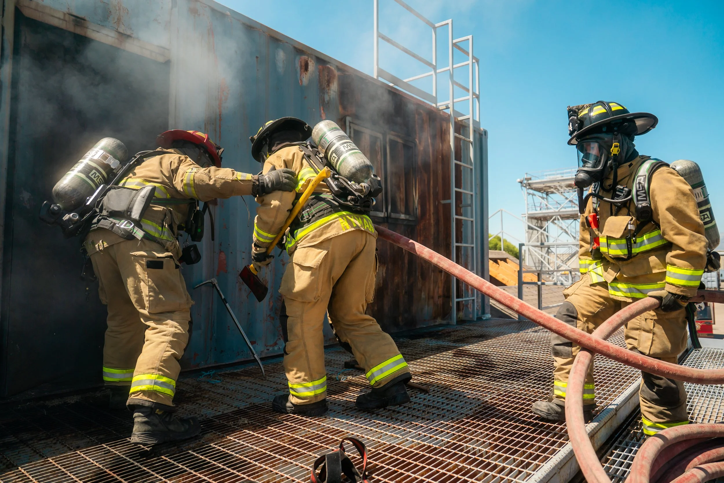 A group of three firefighters start to enter a burning building during a training scenario.