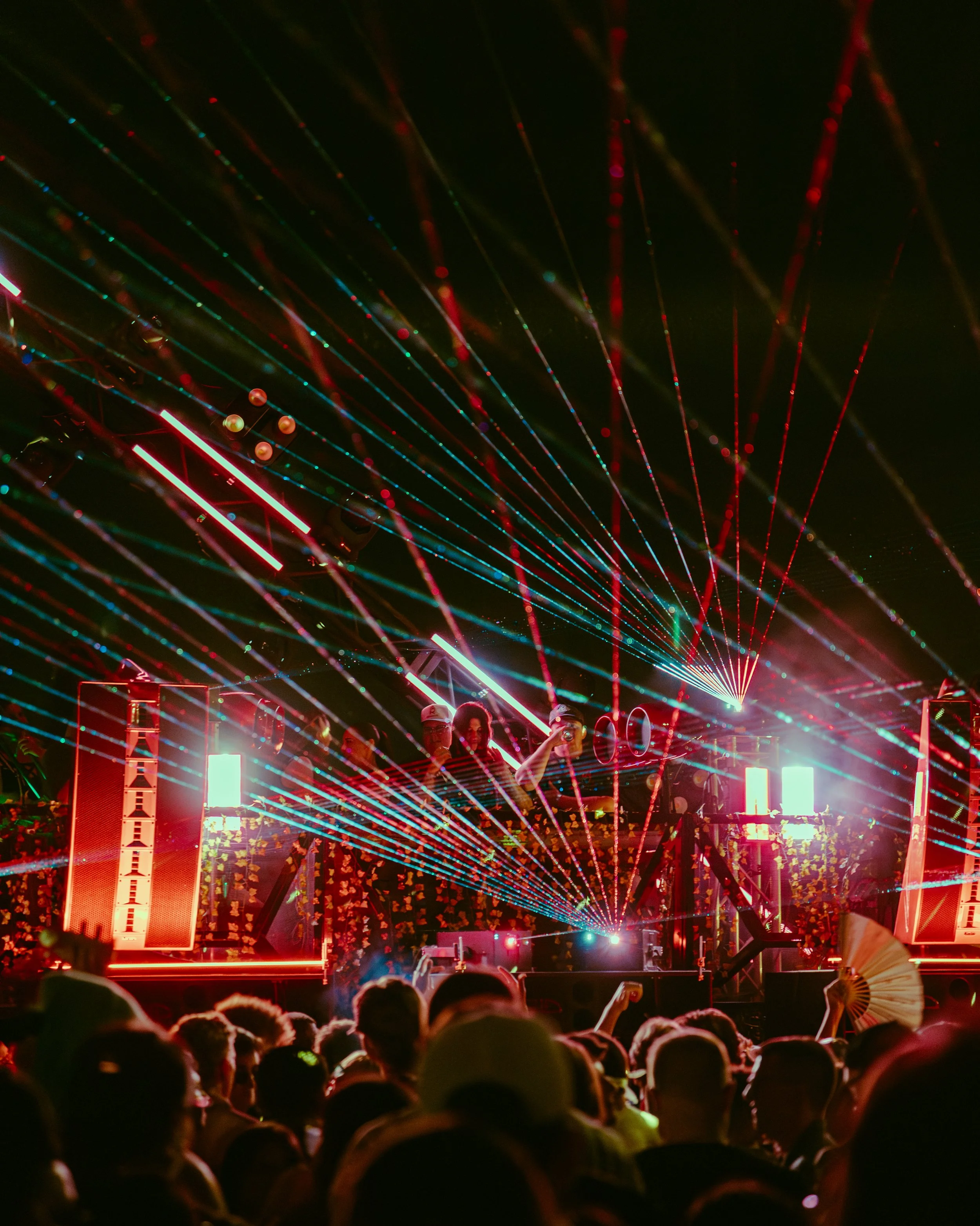 Crowd attending a nighttime outdoor event with colorful laser light beams and lasers lighting up the sky.