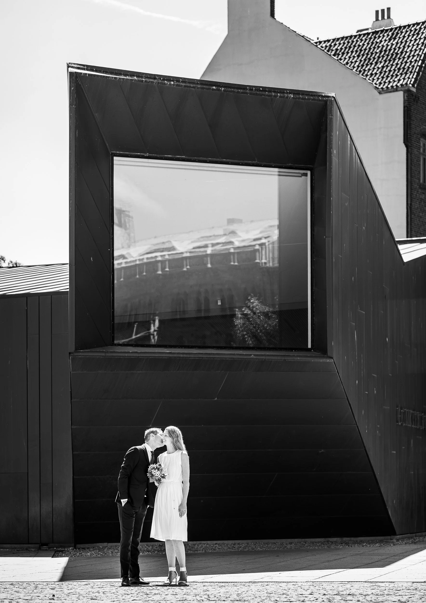 Bröllopsfotografering i Lund. Nyblivet brudpar framför Domkyrkoforums moderna arkitektur med en reflektion av den historiska domkyrkan.