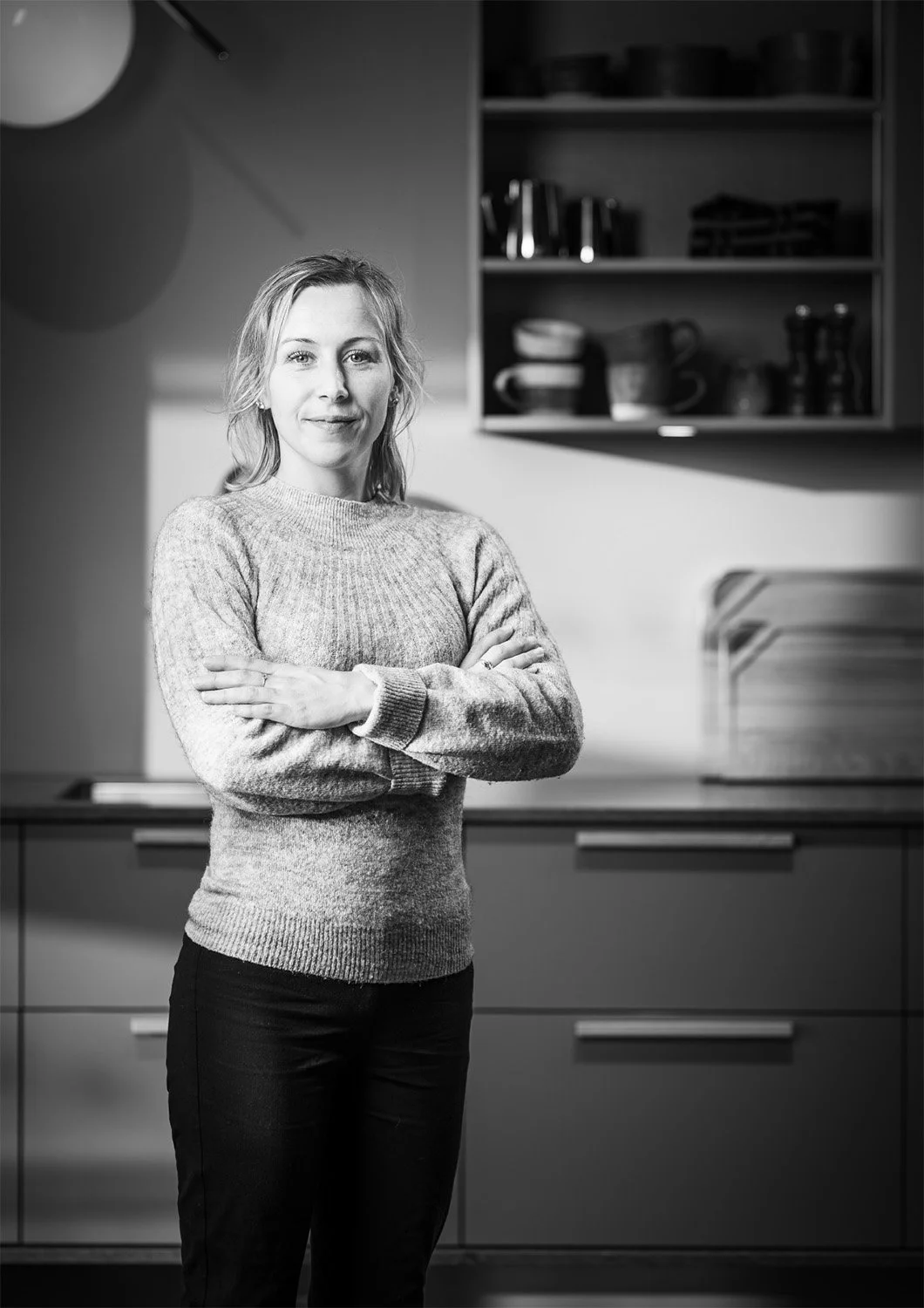 Svartvitt personalporträtt av kvinna med armarna i kors i ett modernt kök