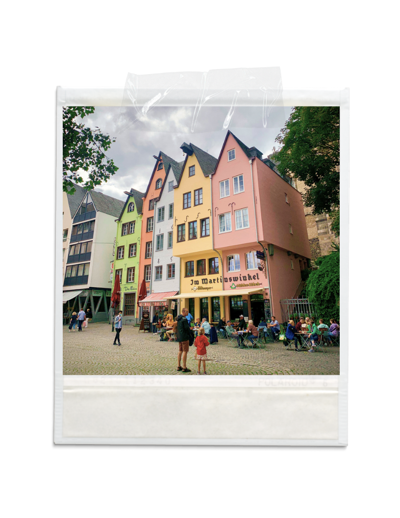 Colorful buildings with outdoor seating and people in a cobblestone square.