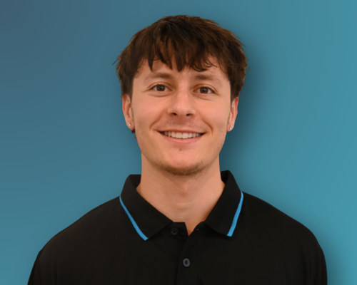 A young man with brown hair wearing a black polo shirt with blue accents, smiling in front of a solid blue background.