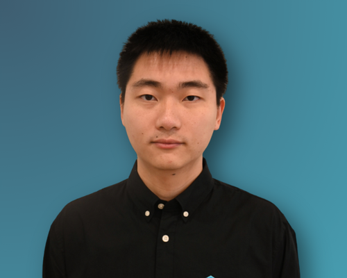 A young Asian man with short black hair, wearing a black collared shirt, standing against a plain teal background.