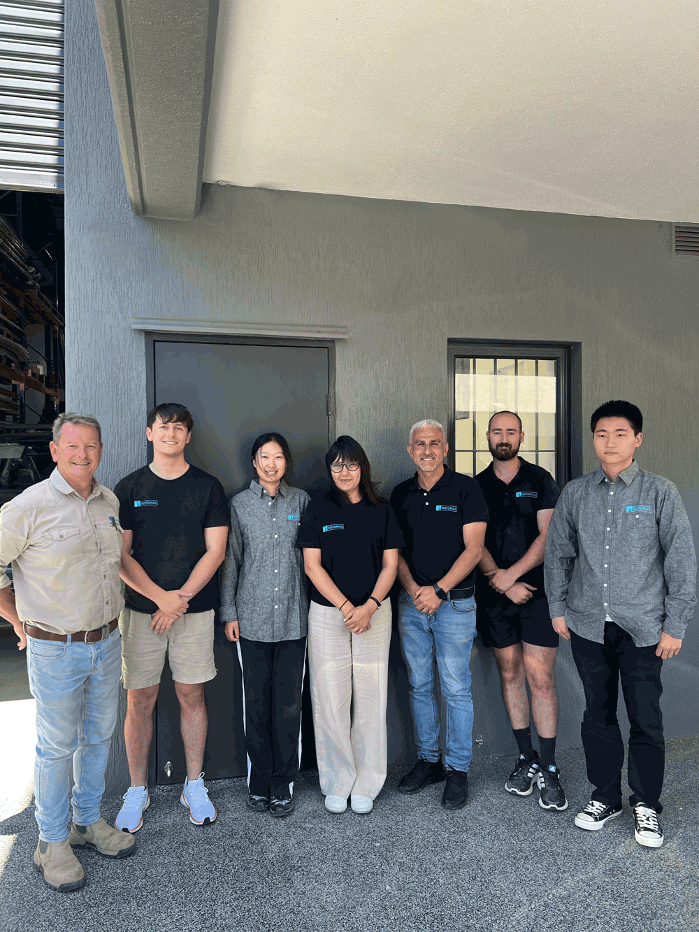 Group of seven people standing side by side outside a building.