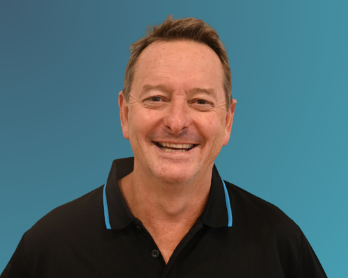 Smiling middle-aged man with short brown hair, wearing a black polo shirt with blue accents, standing against a blue background.