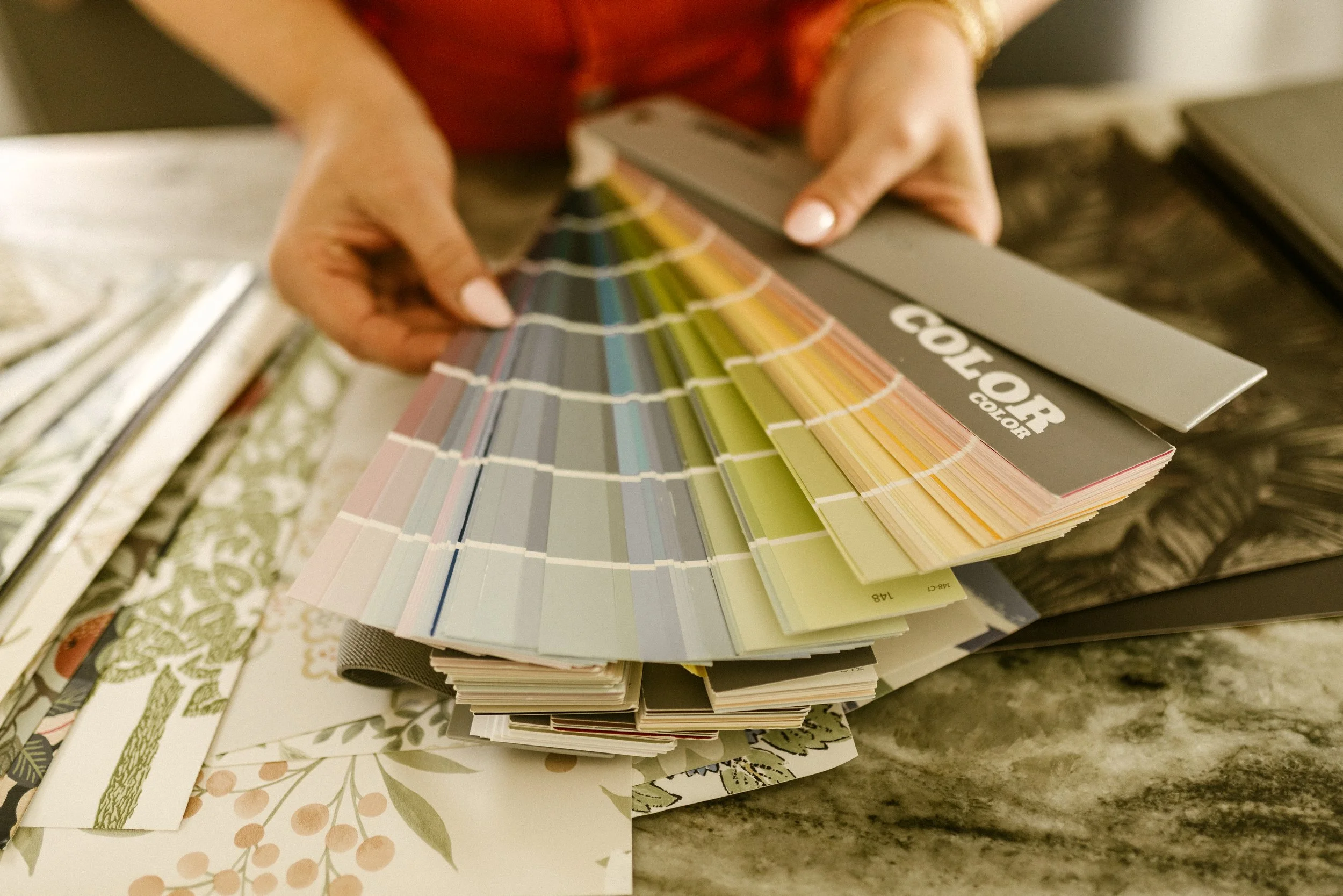 Person flipping through a color sample book, with various paint and fabric color swatches, on a marble surface.