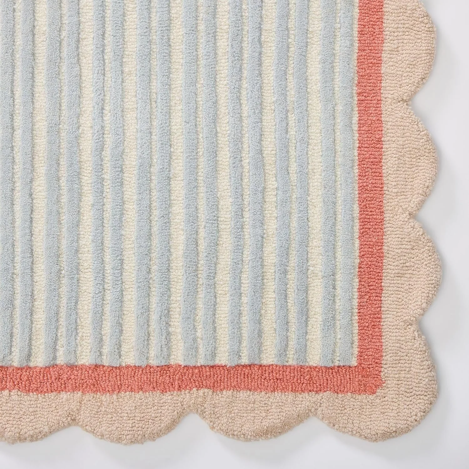Close-up of a rectangular, scalloped-edge, striped rug with pastel blue, beige, and coral colors, showing detailed woven texture.