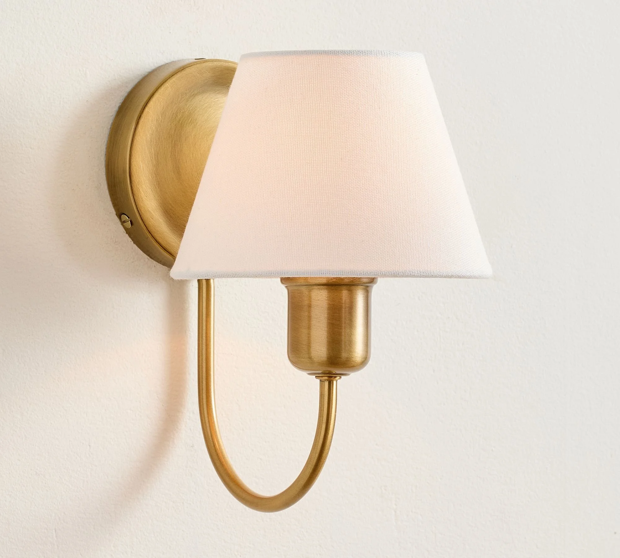 Wall-mounted gold sconce with a white lampshade