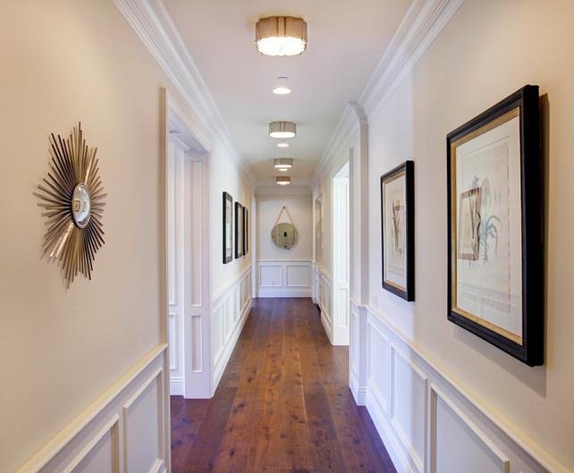 white hallway with wainscoting with mildly dark wood floors, modern wall art, vintage inspired ceiling lights, bright white crown moulding, and a beautifully cohesive look
