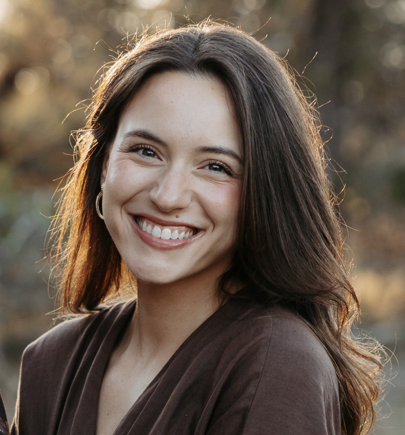 Owner and SLP Scout Johnson, smiling outdoors during golden hour, in a brown top.