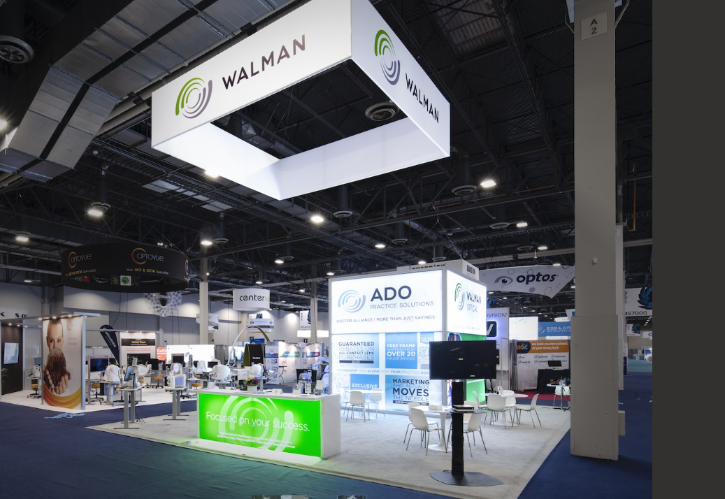 Trade show booth for Walman featuring signage, digital displays, and chairs in a large exhibition hall.