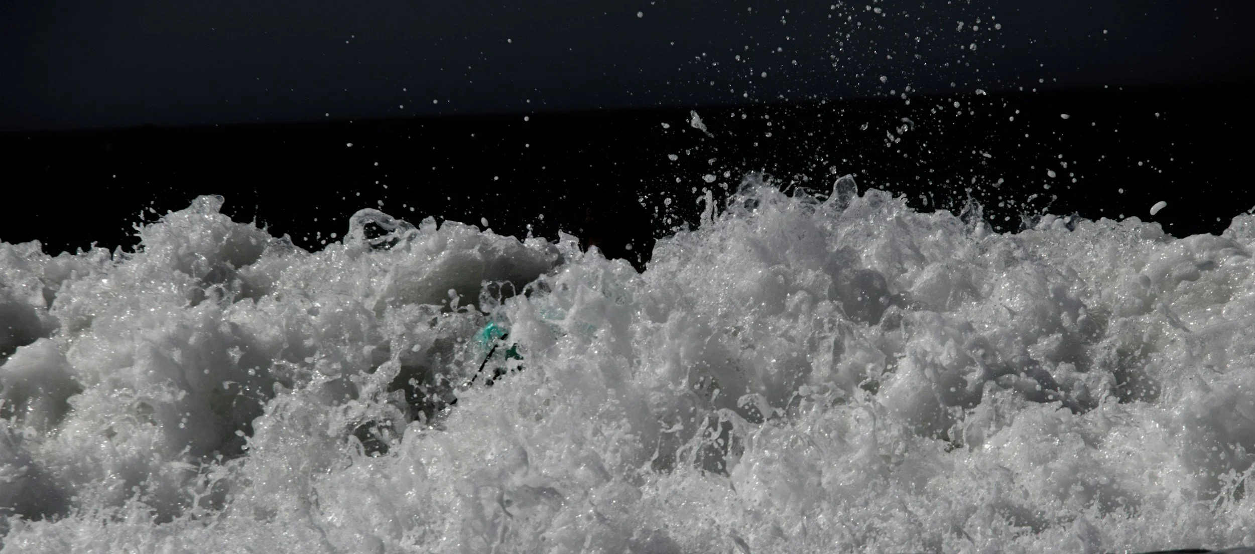 Crashing ocean waves with white foam and dark sky in the background.