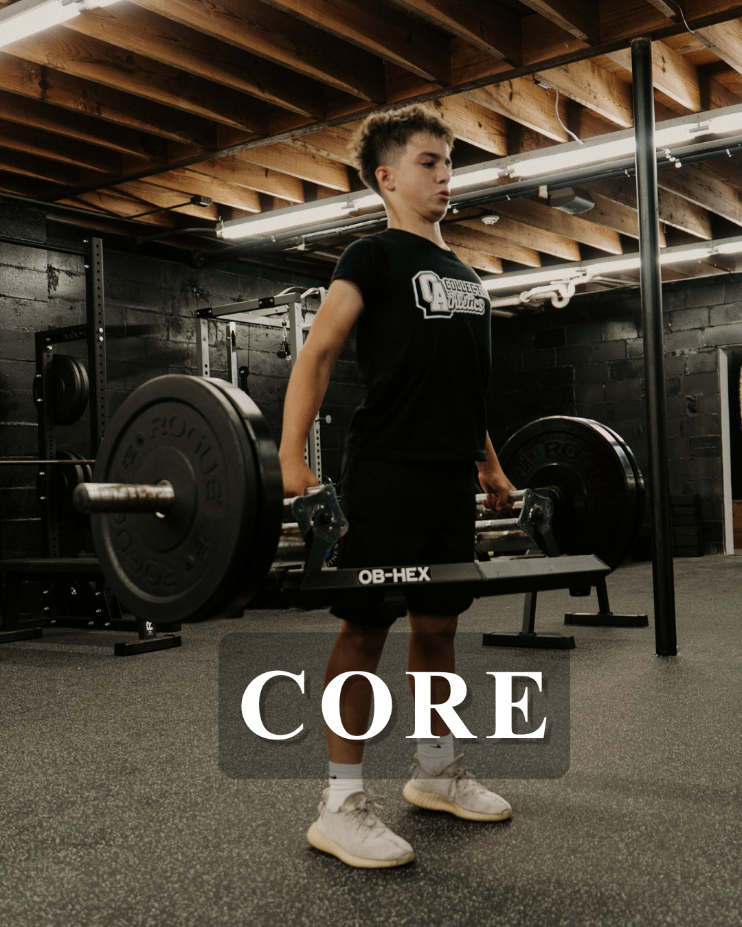 A young boy lifting a barbell in a gym with black walls and wooden ceiling, wearing a black t-shirt and shorts, with the word 'CORE' written across the image.