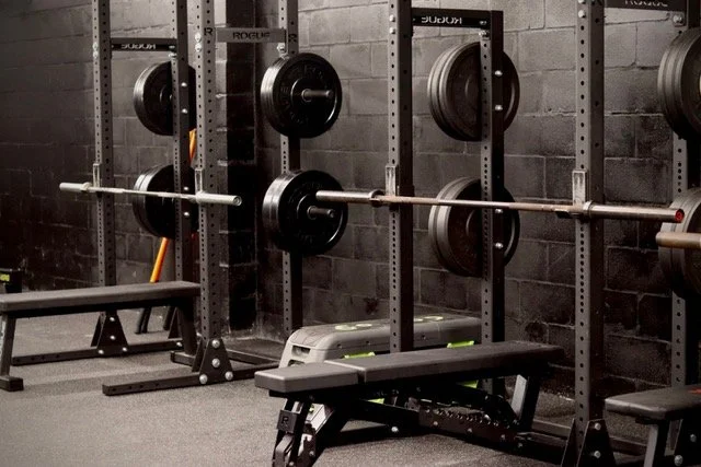 Weightlifting equipment in a gym, including barbells and weight plates on racks.