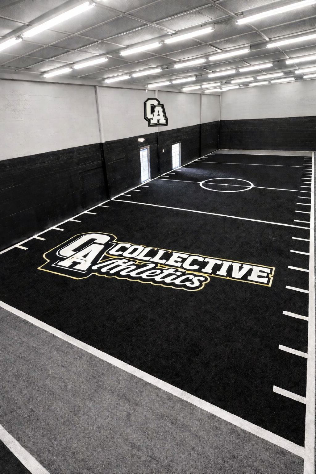 An indoor sports court with black flooring, white boundary lines, and a central circle, featuring the logo and name of 'Collective Athletics' on the floor and a large 'A' logo on the wall.