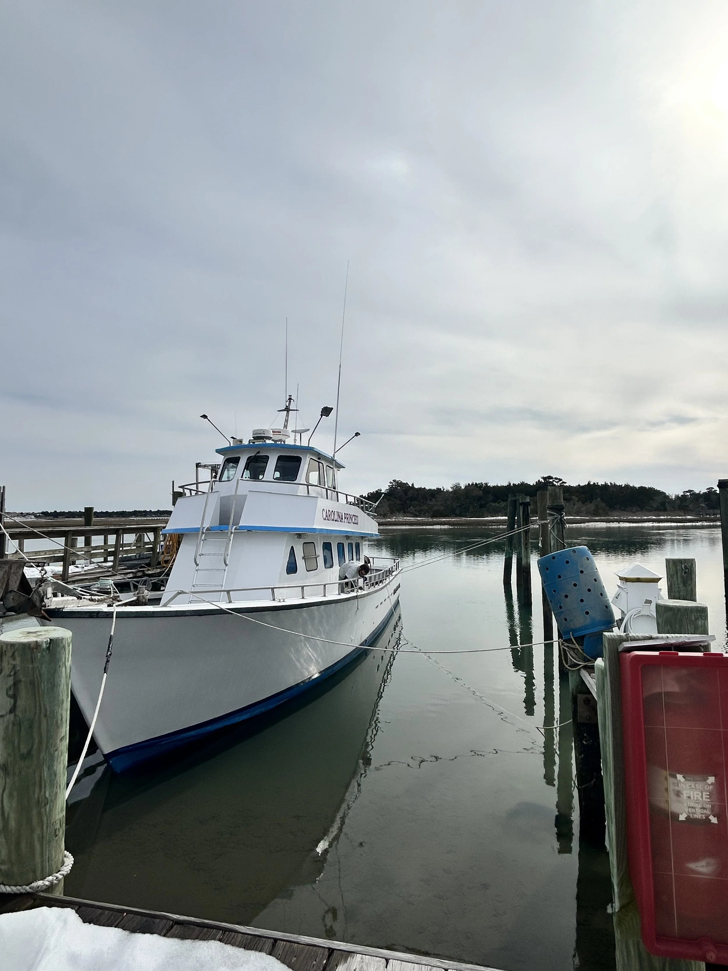 A white boat docked at a marina pier under a cloudy sky with trees in the background.