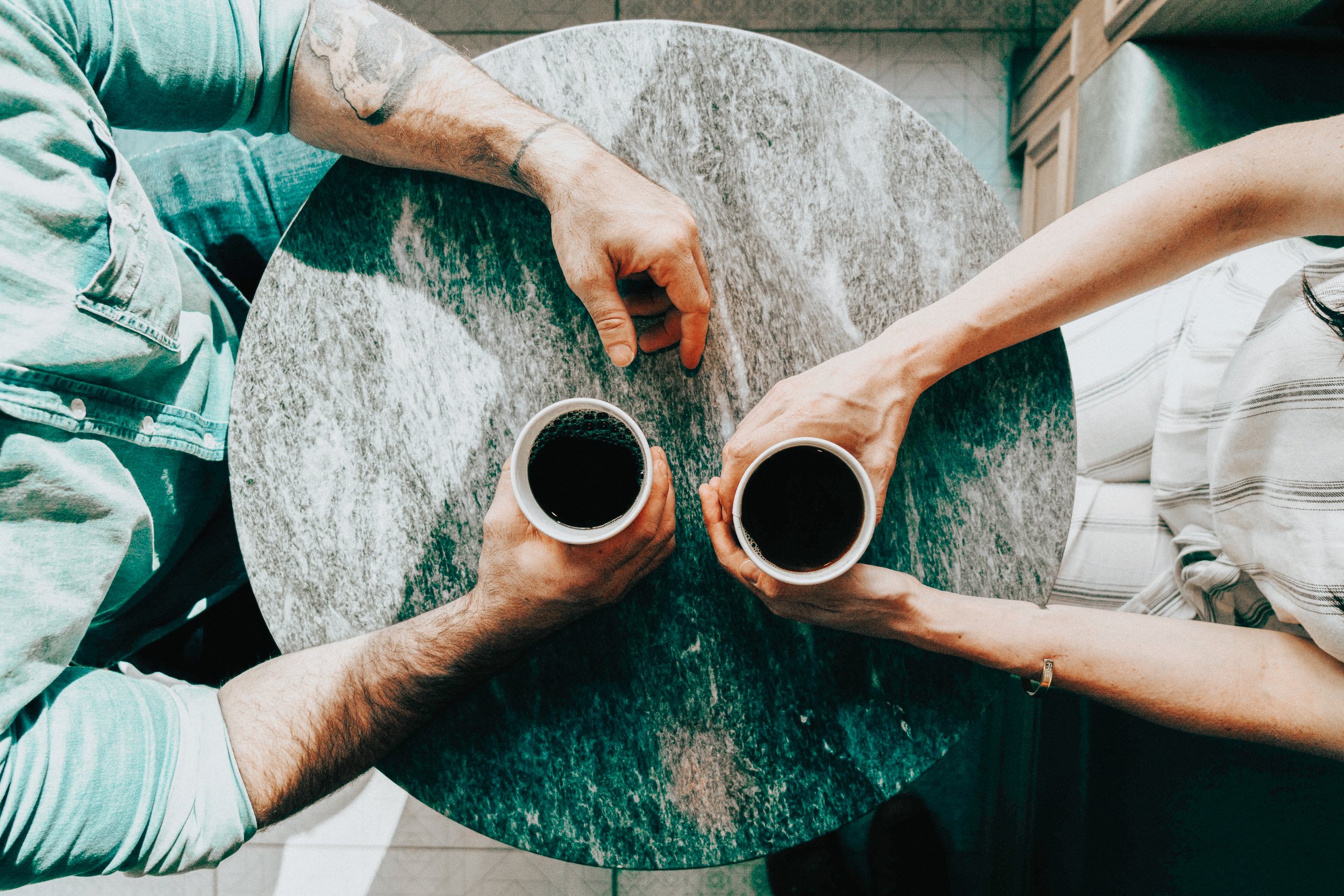 Two people sitting at a round table, each holding a cup of coffee, viewed from above.