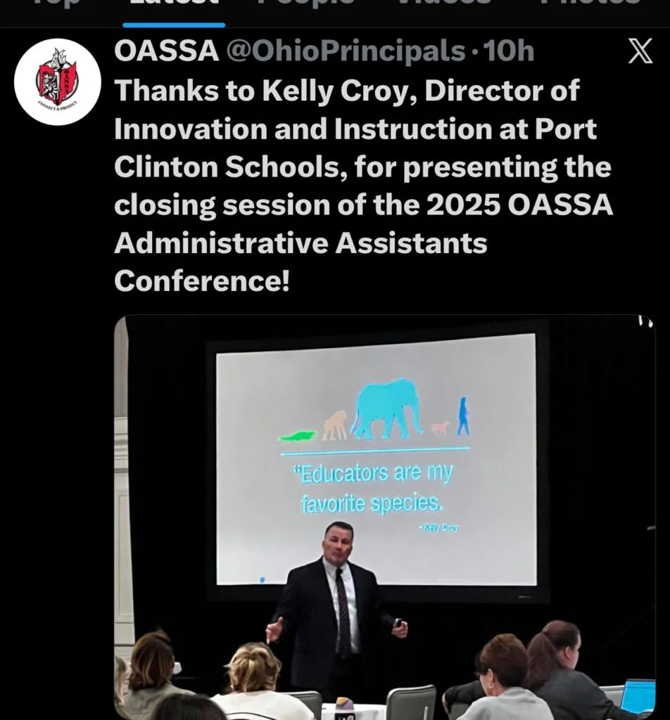 A man in a suit speaking at a conference with a large screen behind him displaying a quote and animal silhouettes. The quote reads, "Educators are my favorite species" attributed to Kelly Croy.