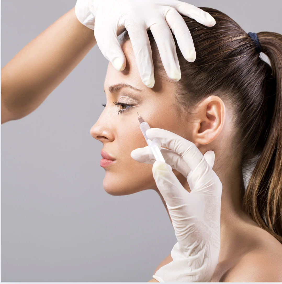 A woman receiving a cosmetic injection in her face by a healthcare professional wearing gloves.