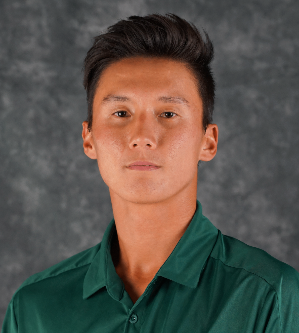 Headshot of a young man with dark hair, wearing a green collared shirt, against a gray textured background.