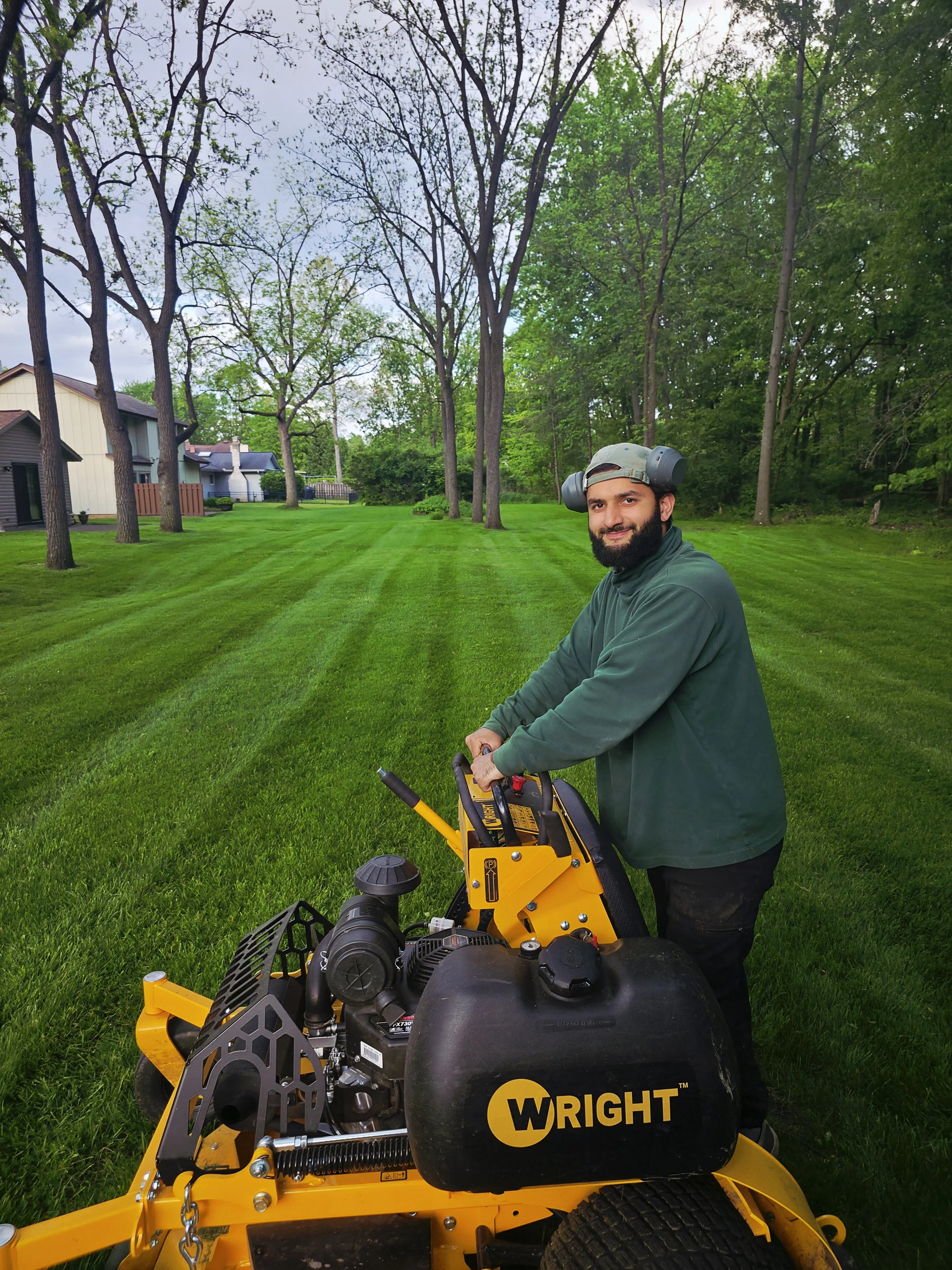 A business owner on a commercial lawn mower smiling with grass cut in the background