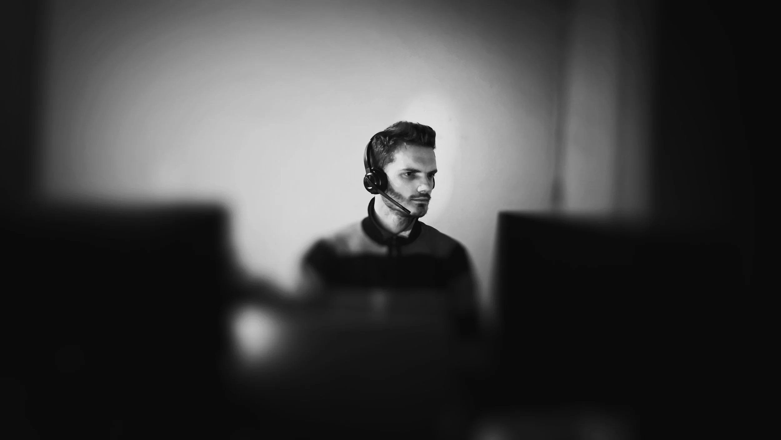 A black and white photo of an entrepreneur working late at night with a headset, staring at multiple computer screens, illustrating the stress and isolation of the 'Operator Cycle' in small business.