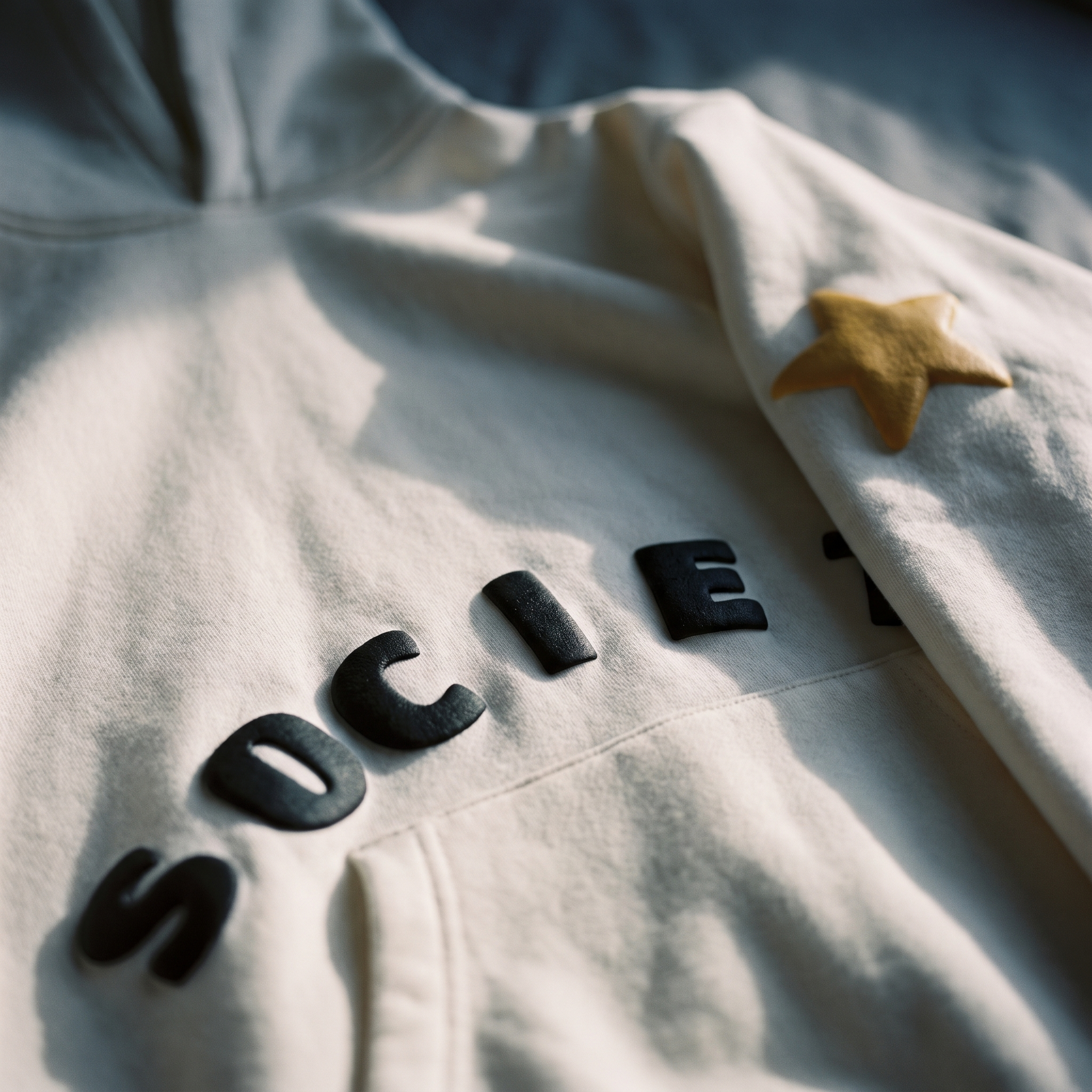 Raised black puff SOCIETY lettering on White Hoodie cotton, with ribbed hem detail.