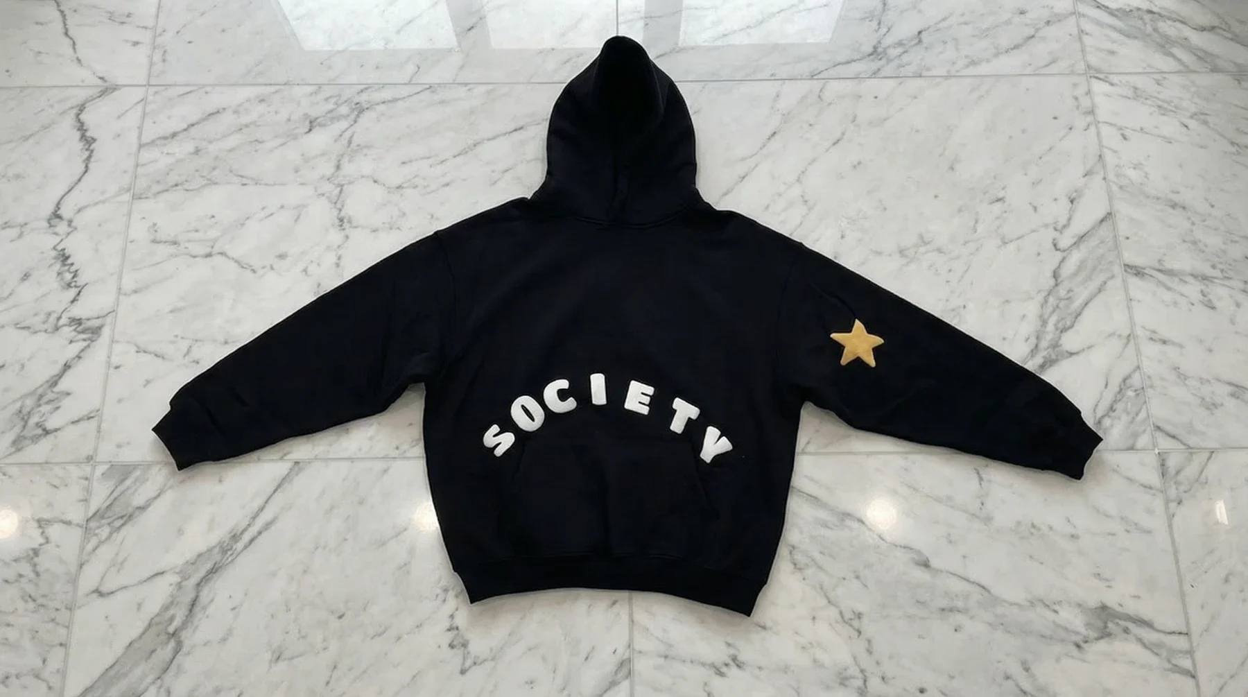 Black hoodie laid flat with white puff lettering and a gold sleeve star.