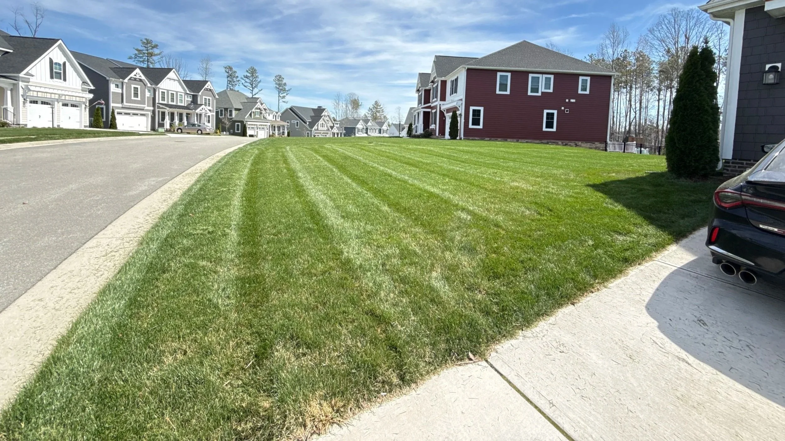 A suburban neighborhood with a row of modern houses, a well-manicured green lawn, and a clear blue sky.