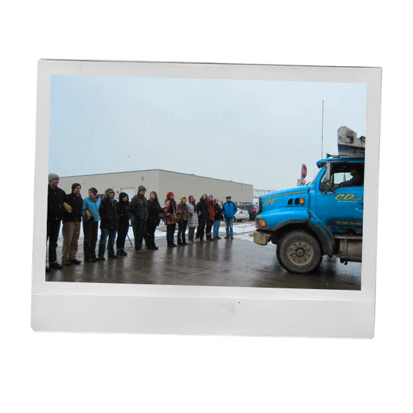 Winona community members standing arm and arm in solidarity together, facing a large blue truck.