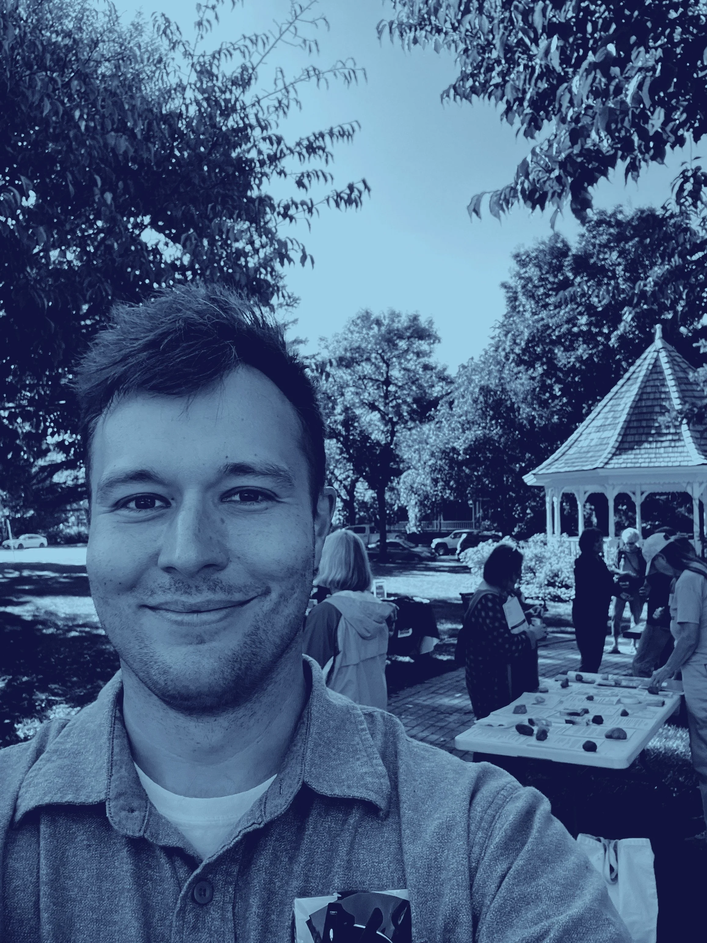 A Dan Wilson selfie of him smiling at  the camera. Behind him is the Windom Park gazebo and people at the John Latch Celebration.