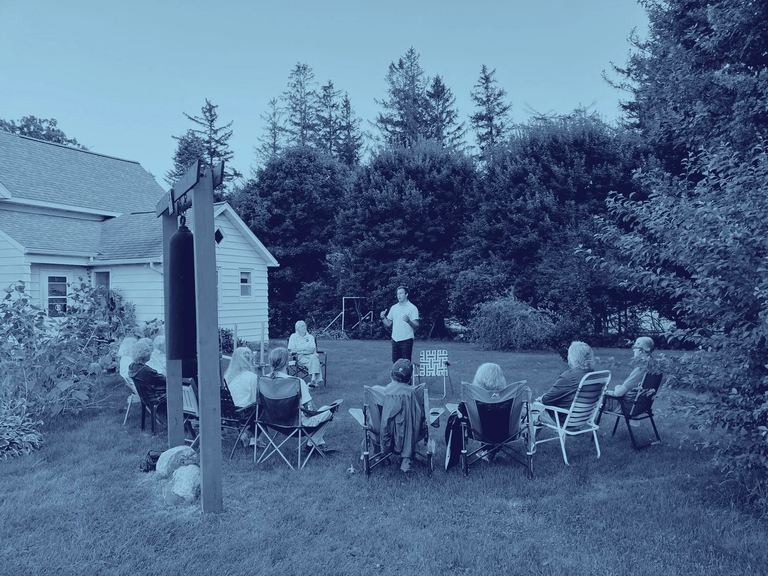 Dan speaking to a group of people sitting in lawn chairs in a circle around him. They're outside in someone's yard.