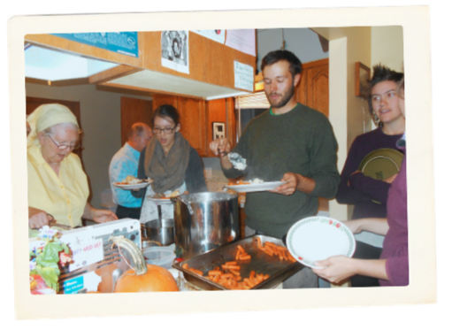 Dan Wilson in Bethany House standing in the kitchen serving food. There are many people around him working.