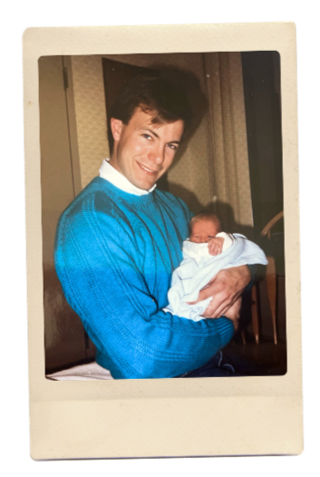 An aged photo of Dan Wilson's young father wearing a blue sweater and holding a baby in his arms.