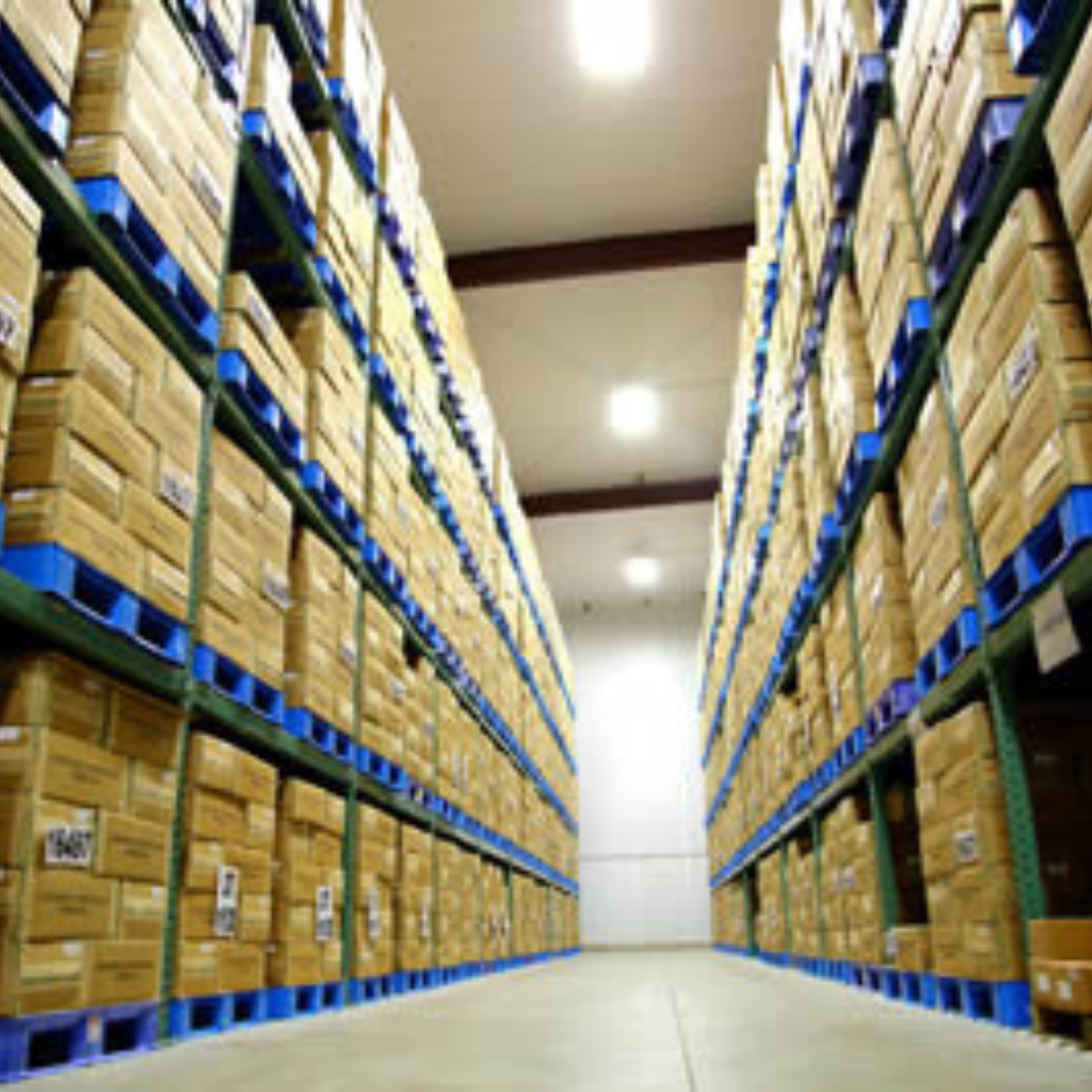 Warehouse aisle with tall shelves stacked with cardboard boxes on blue pallets.
