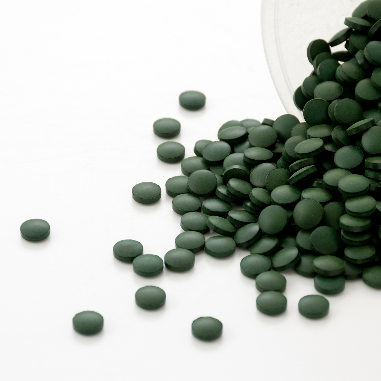 Small green tablets spilling out of a container onto a white surface.