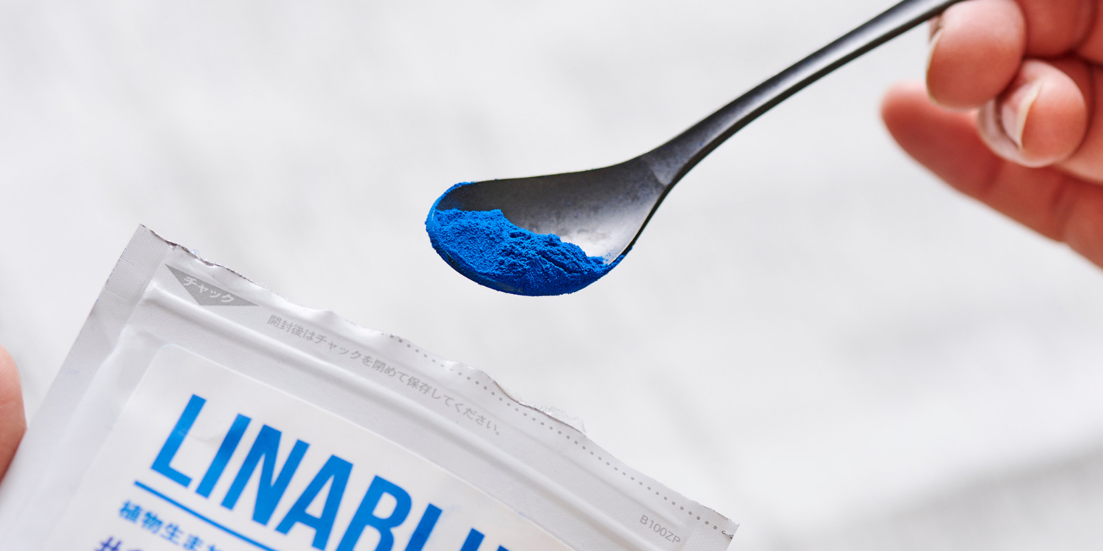A spoon with bright blue powder being held above a white packet labeled "LINAR" in blue text.