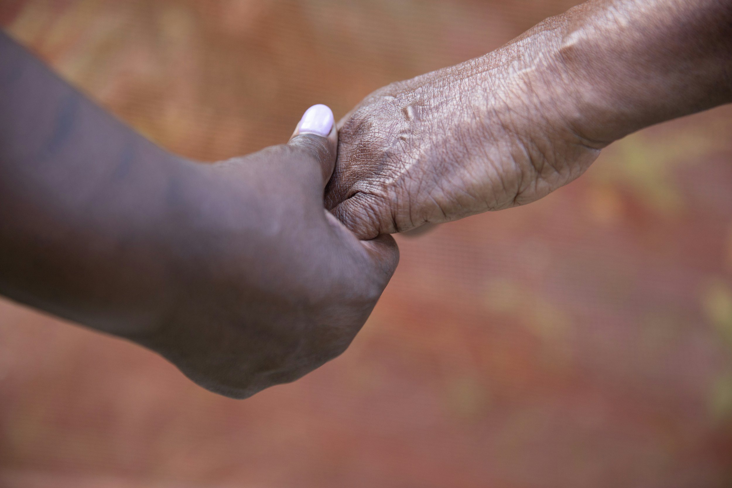 Two hands, one darker-skinned and the other light-skinned, holding each other's fingers.