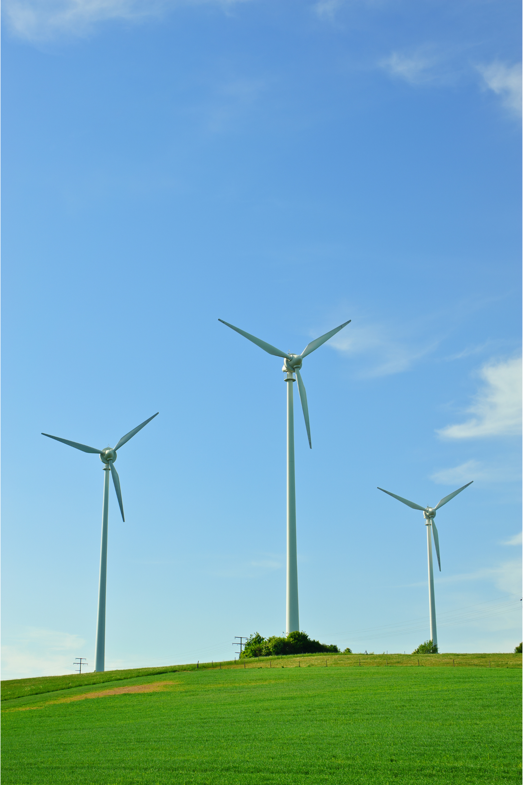 Three wind turbines on a grassy hill under a blue sky with some clouds.
