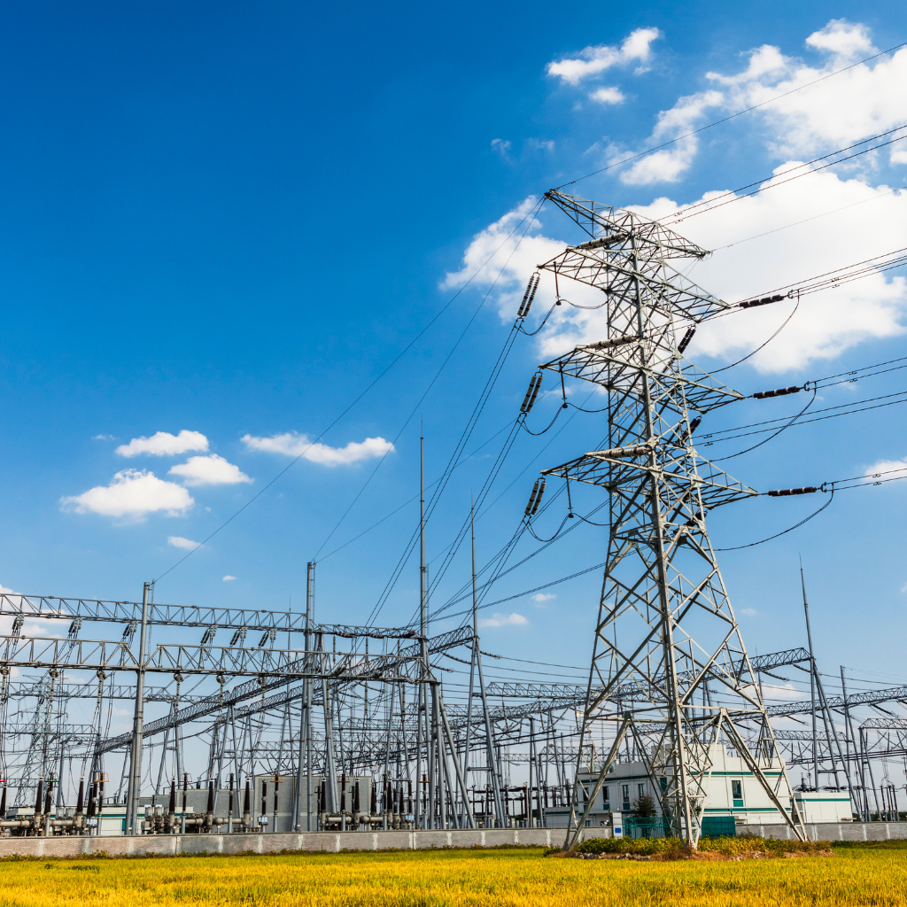 Electrical power transmission towers and lines in a field under a blue sky with scattered clouds.