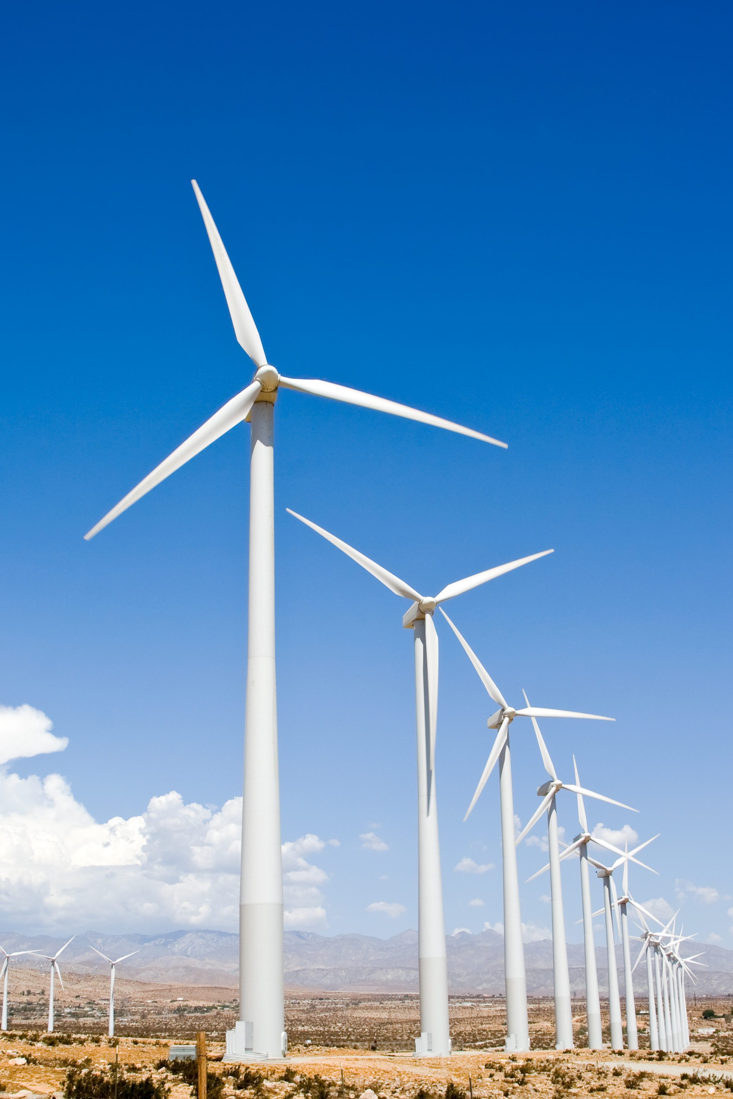 Wind turbines in a desert landscape with mountains in the background and a clear blue sky.