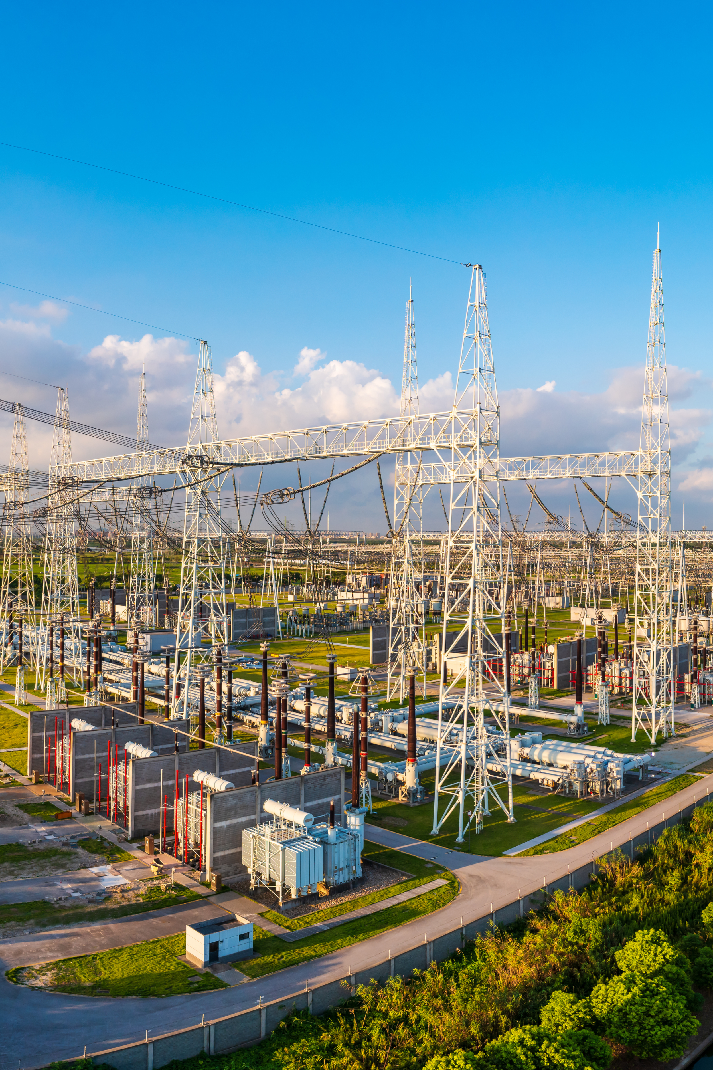 An electrical substation with metal towers, transformers, and power lines under a blue sky with scattered clouds.