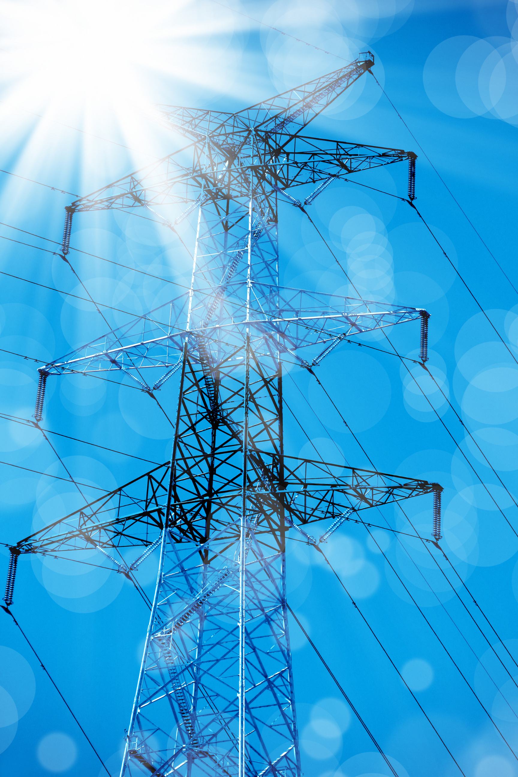 Cột truyền tải điện cao thế nổi bật trên nền trời xanh với ánh nắng chói chang và hiệu ứng lóe sáng ống kính.