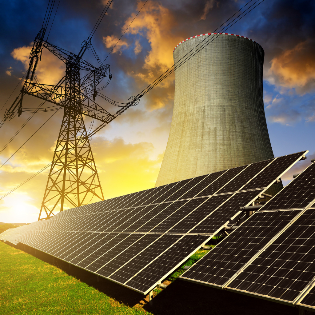 Solar panels in the foreground with a nuclear cooling tower and high voltage power lines in the background during sunset.