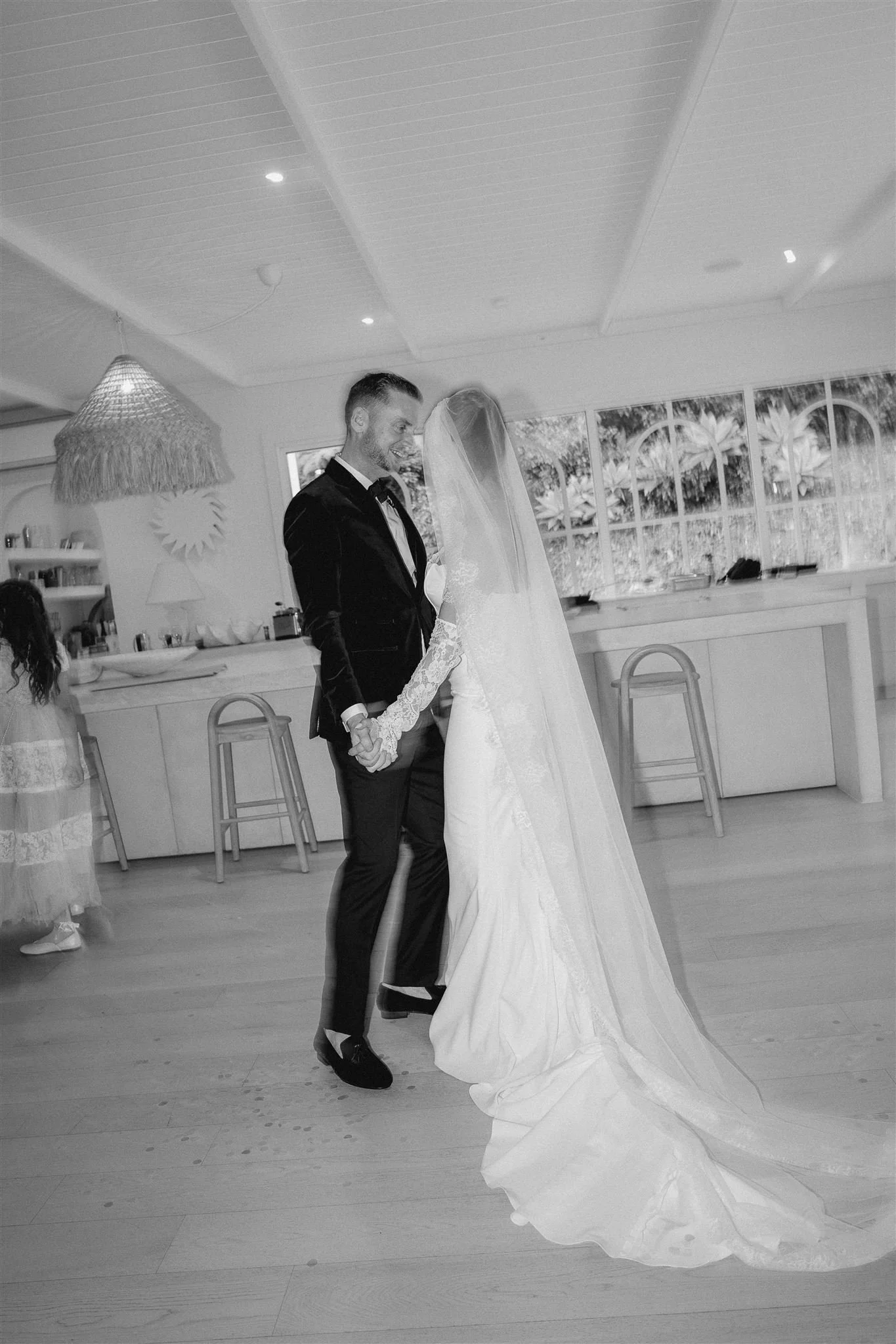 A groom and bride holding hands during a wedding dance in a bright, decorated room.