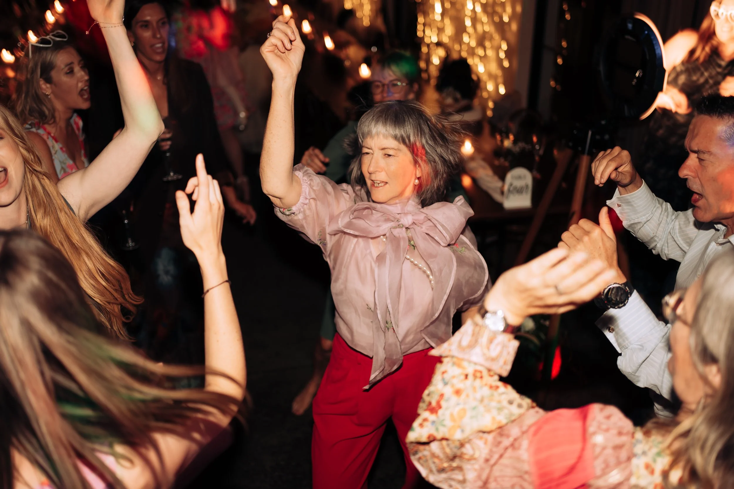 People dancing and enjoying at a lively party with warm lighting and string lights in the background.